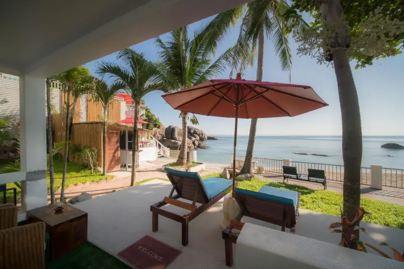 Sun loungers under a parasol on the beachfront lawn, looking out to the bay